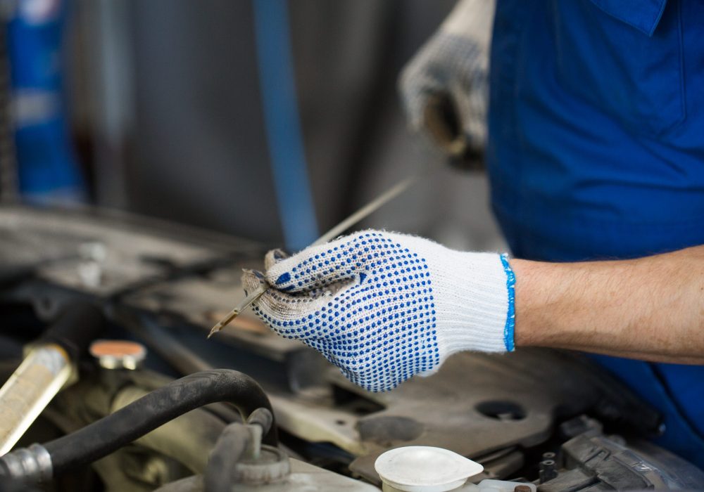 car service, repair, maintenance and people concept - auto mechanic man with dipstick and lamp checking for motor oil level at workshop